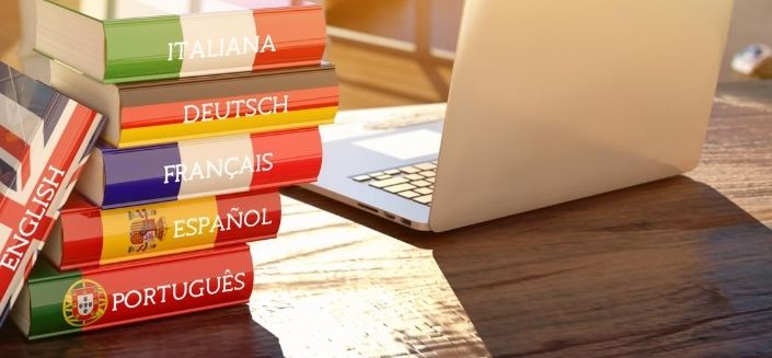 A stack of dictionaries in several languages next to a laptop to illustrate translation