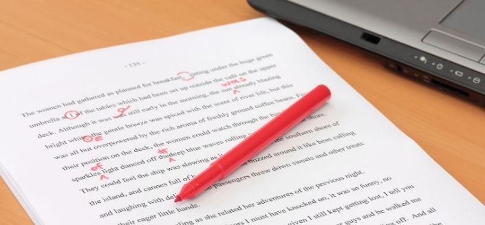 Documents with red pen corrections next to a laptop to illustrate proofreading